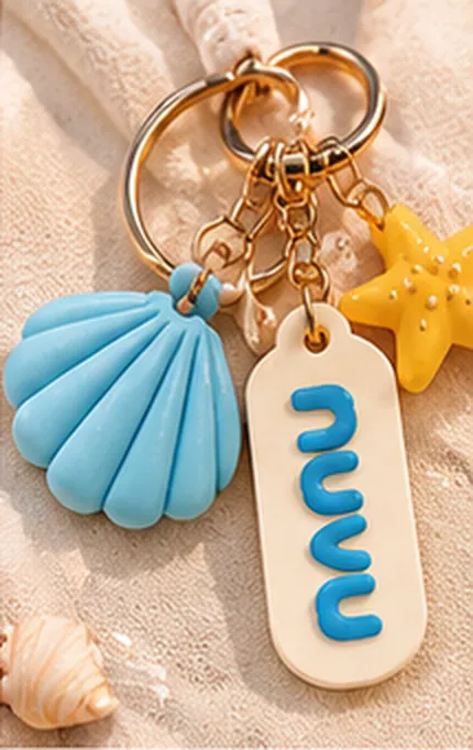 Chaveiro com concha azul, estrela e plaquinha sobre a areia